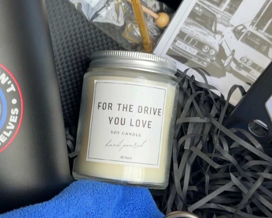 Candle labeled 'For the Drive You Love' in a gift box with other items.