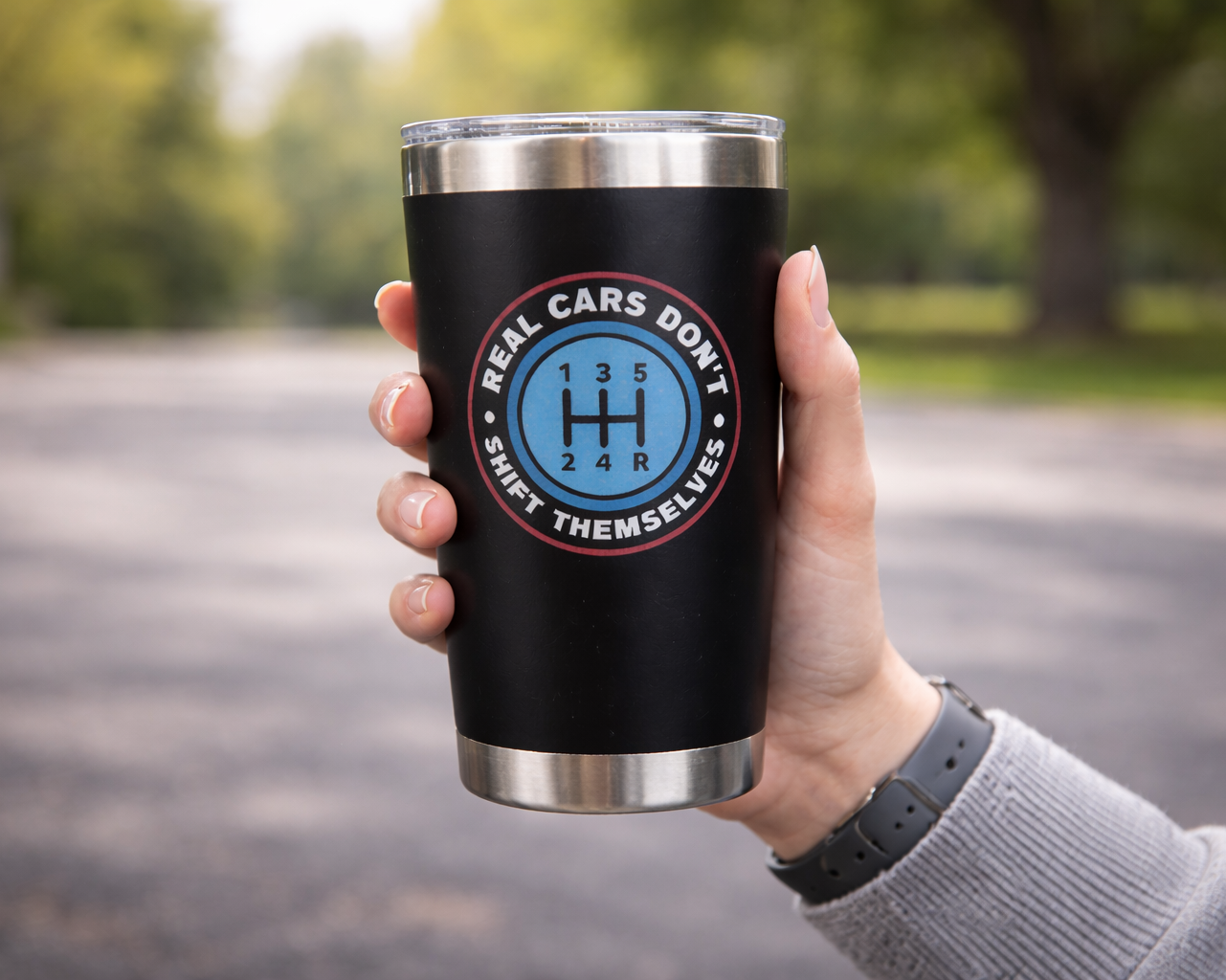 Black tumbler with a design held by a hand outdoors