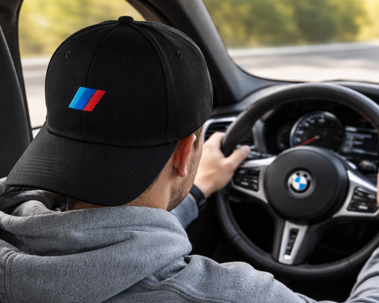 Person driving a BMW car wearing a black cap with a logo.