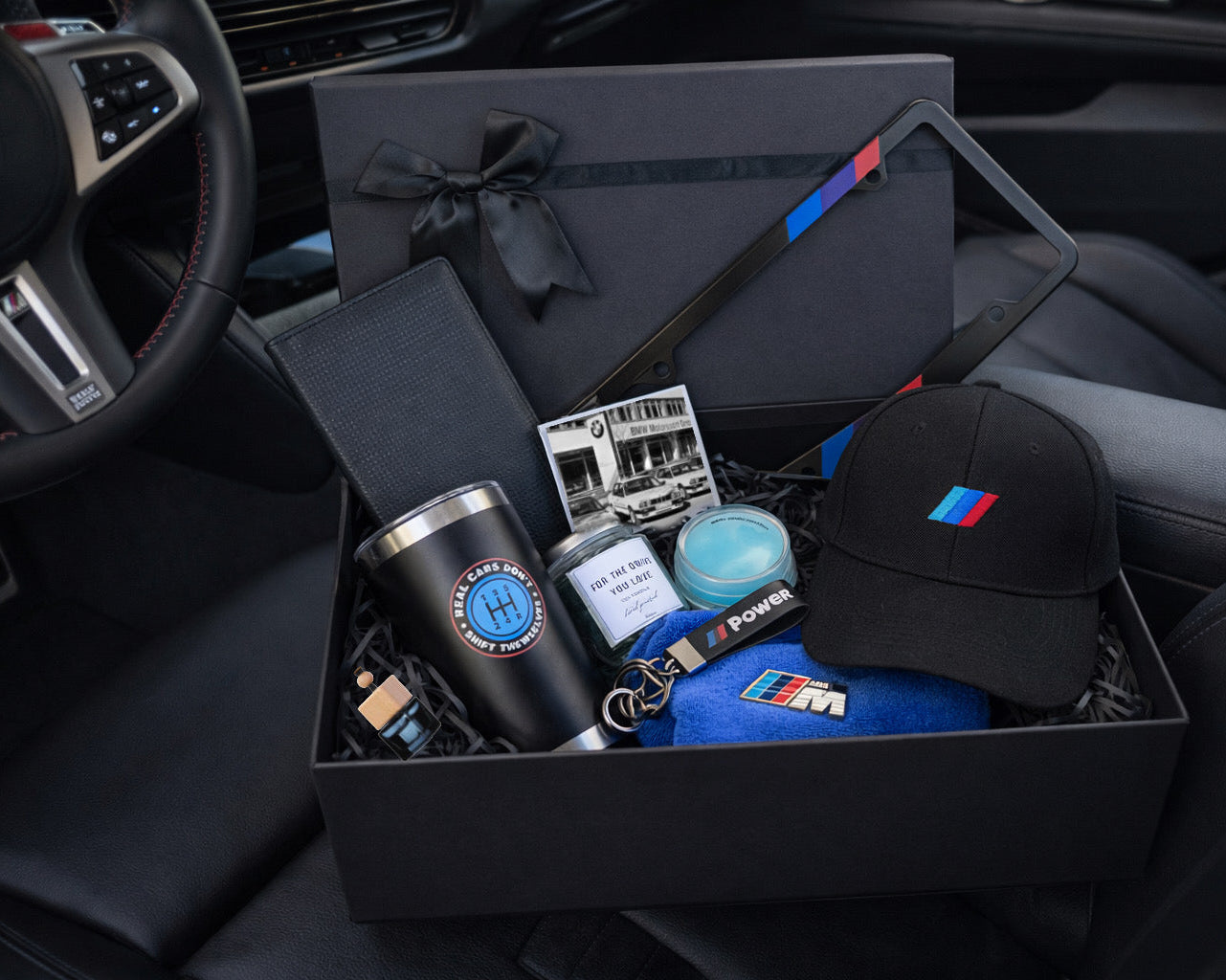 Gift box with BMW-themed items including a cap, tumbler, and keychain inside a car.