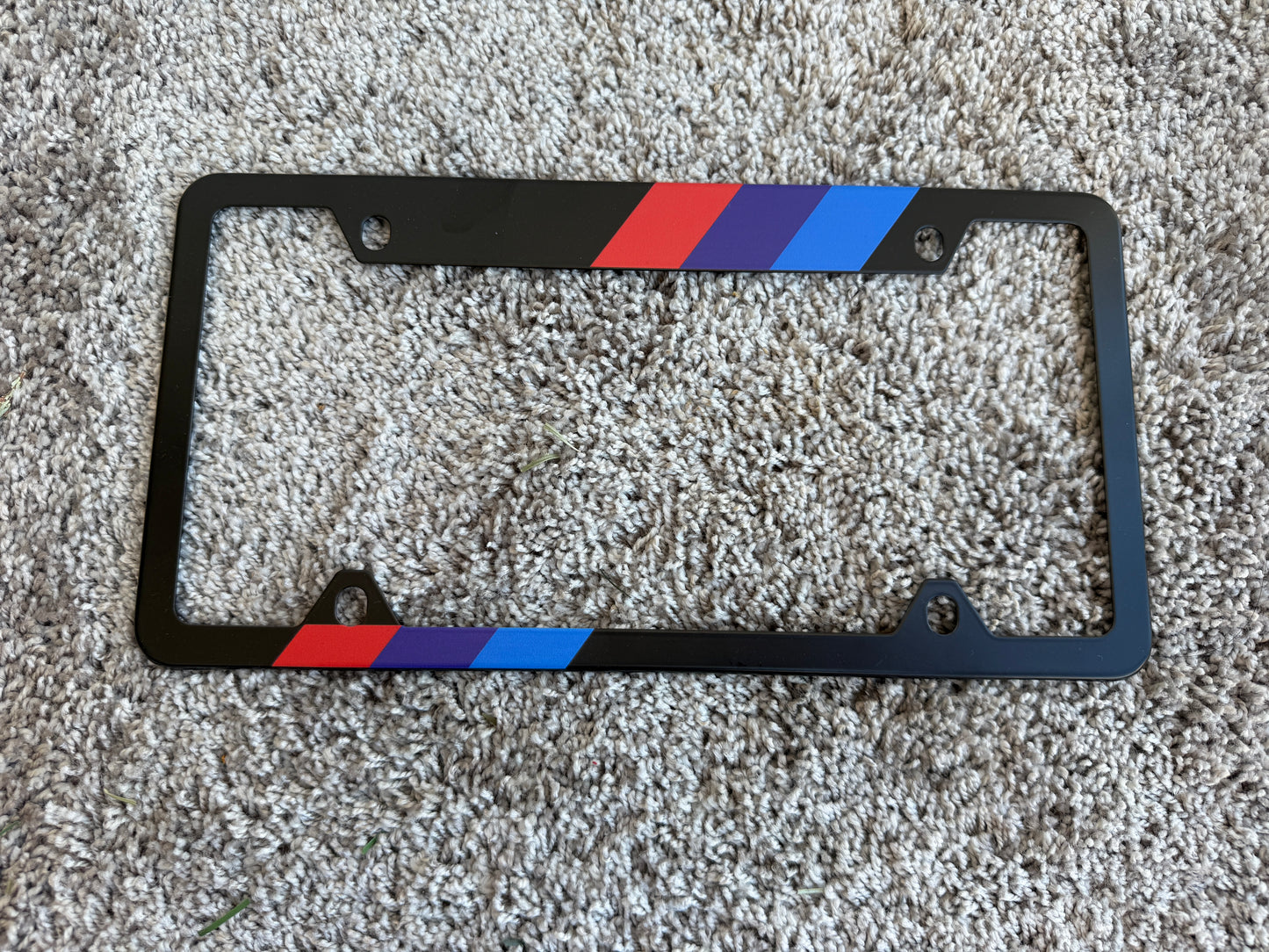 Black license plate frame with red, blue, and white stripes on a textured surface