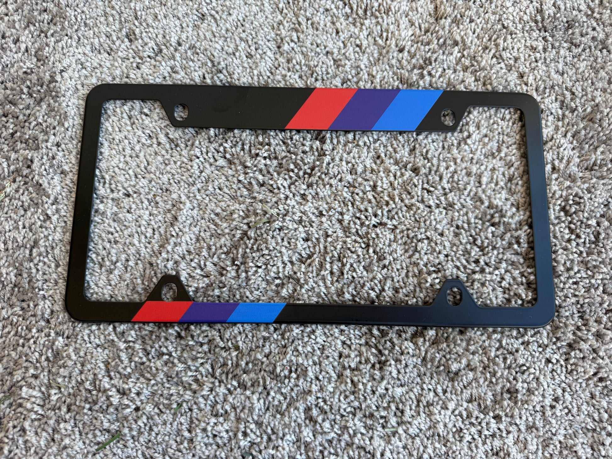 Black license plate frame with red, blue, and white stripes on a textured surface